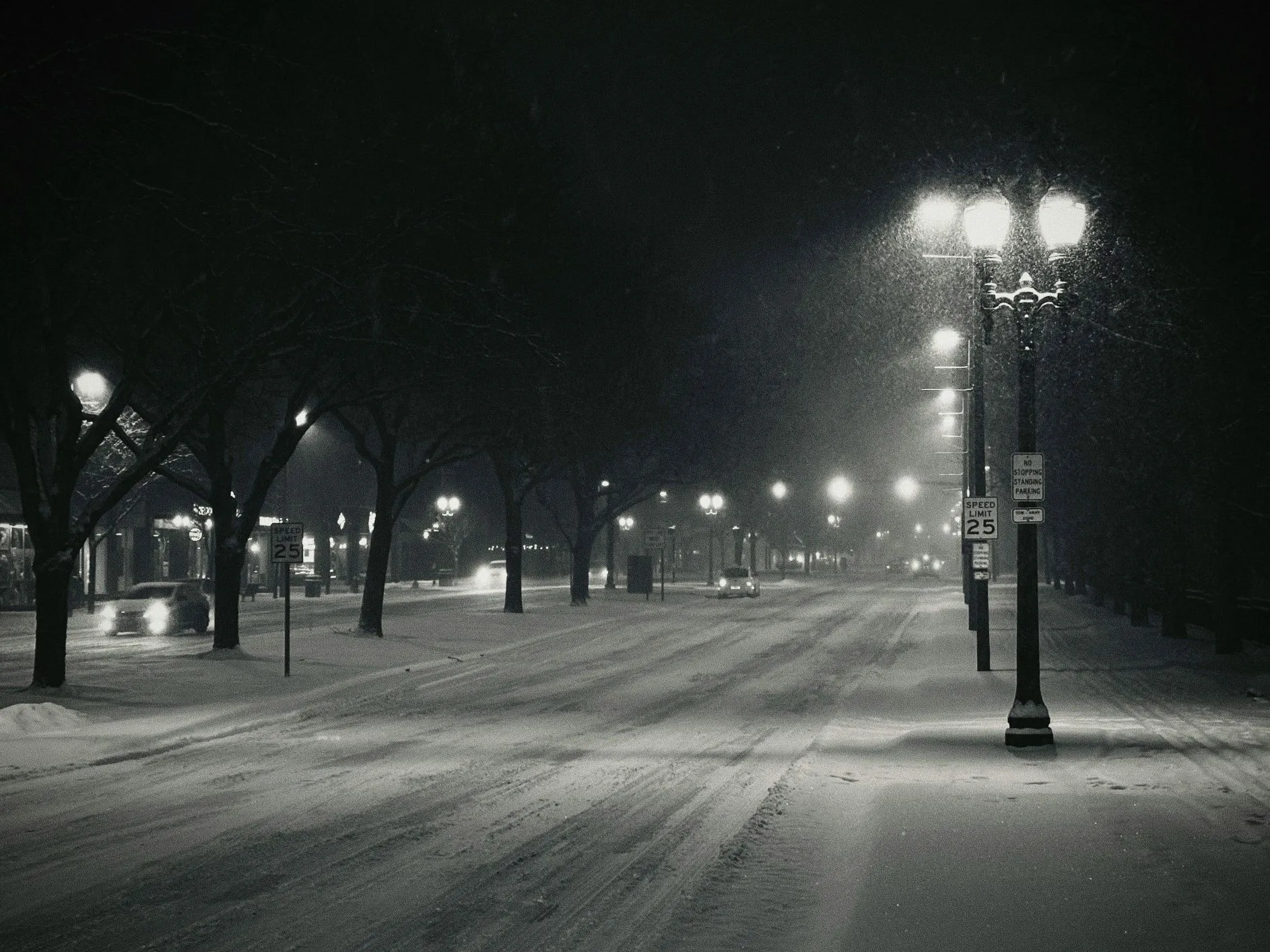 East Lansing street on a snowy winter night, with cars and streetlights glowing through the falling snow, a quiet Michigan evening scene.